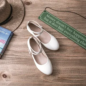 Detailed top view of elegant white Mary Jane shoes with cross straps on wooden surface