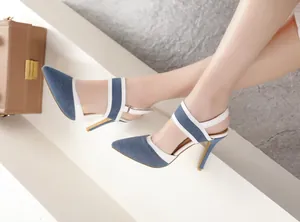 Detalle de primer plano de sandalias de tacón de aguja en mezclilla azul con correas blancas.