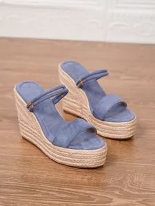 Primer plano de sandalias de cuña en ante azul con plataforma de cuerda de paja natural.