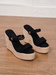 Primer plano de sandalias de cuña negras con plataforma de paja trenzada y detalle oro