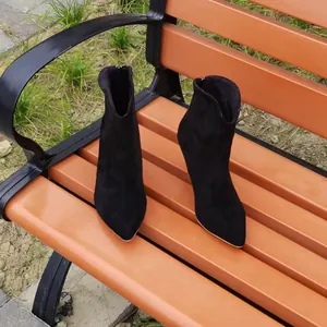 Macro view of black pointed toe high heel ankle boots displayed on an outdoor park bench.
