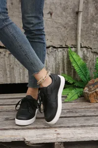 Modische schwarze Damen-Sneaker zum Schnüren mit dicker weißer Sohle auf Holzboden