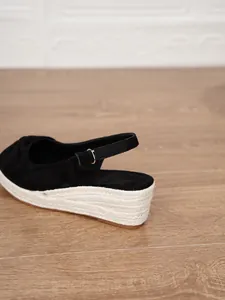Detailed side view of black suede wedge sandal featuring espadrille sole and ankle strap