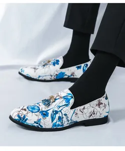 Close-up of men's white loafers featuring a vibrant blue floral print and metal tassels.