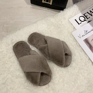 Close-up detail of grey cross-strap faux fur slippers presented on a white shaggy rug