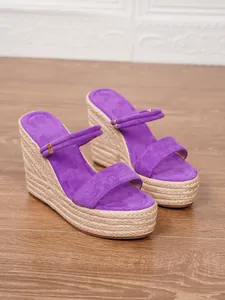 Detalle de sandalias con cuña de ante morado y suela de plataforma de esparto tejida.