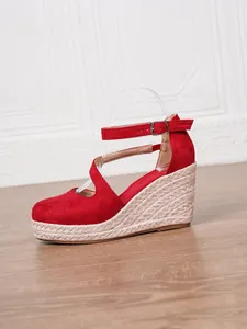 Détail des sandales compensées en daim rouge avec semelle en corde et bride à la cheville.