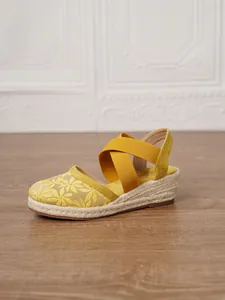 Primer plano de sandalias de cuña tipo alpargata amarillas con bordado floral fino