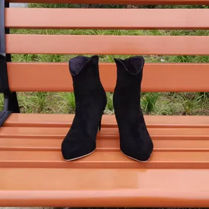 Elegant black faux suede pointed-toe stiletto ankle boots displayed on a park wooden bench