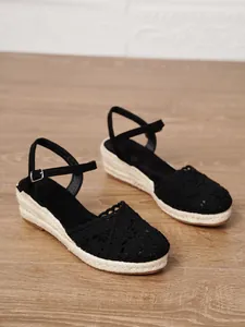 Elegantes sandalias de cuña con ganchillo negro para mujer sobre un suelo de madera natural