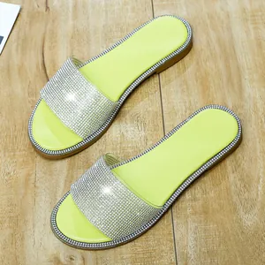 Detailopname van neongele platte slippers met sprankelende bandjes met strassteentjes