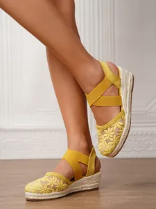 Detalle de alpargatas de cuña amarillas con malla bordada de flores y correas elásticas