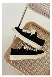 Vista laterale di sneaker in tela nera retrò con spessi lacci crema su sedia di paglia