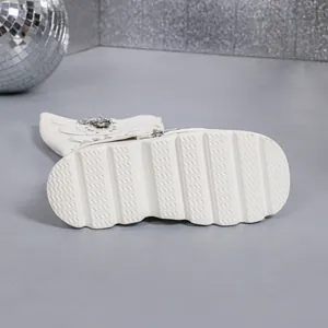 Gros plan de bottes blanches à plateforme montrant la semelle et les boucles gothiques.