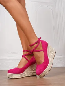 Primer plano de sandalias de cuña fucsia con plataforma de esparto trenzado y correas.