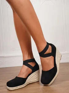 Primer plano de sandalias de cuña tipo alpargata de ante negro con correas elásticas cruzadas.