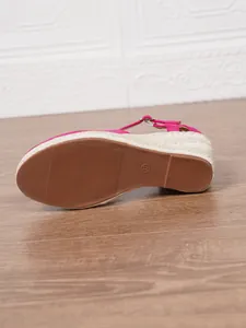 Dettaglio ravvicinato della suola in gomma marrone di un sandalo rosa scamosciato con zeppa