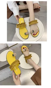 Detail of yellow flat sandals featuring ruffle straps and pearl pineapple embellishments.