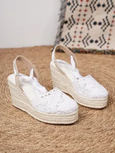 Detalle de sandalias de cuña de ganchillo blanco sobre una alfombra de paja