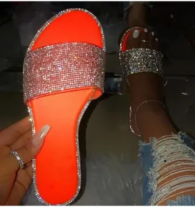 Détail de claquettes d'été orange fluo avec brides ornées de strass brillants de luxe.