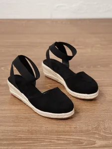Detalle de sandalias de cuña de esparto negras con correas elásticas en el tobillo.