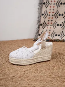 Detalle de sandalias de cuña espardeñas de encaje blanco con cintas en el tobillo.