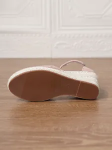 Primer plano de la suela de goma y la cuña de esparto trenzado de una sandalia rosa.