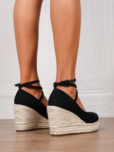 Detalle de sandalias de cuña en ante negro con plataforma de esparto y correas