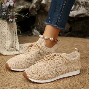 Close-up of beige crochet lace mesh sneakers with intricate spiral patterns on straw mat.