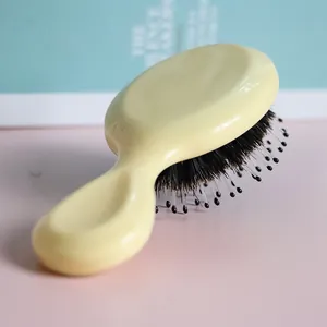 Close-up of small boar bristle hairbrush with cream handle and massage pins.
