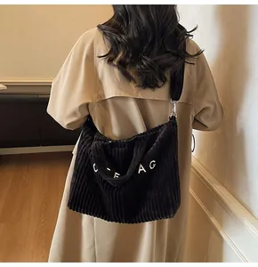 Large black corduroy tote bag shown on a model wearing a beige trench coat