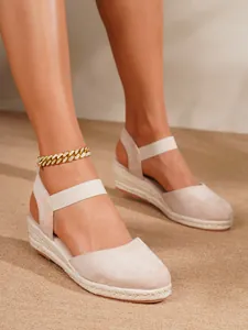 Primer plano de sandalias de cuña tipo esparteña beige con tobillera de cadena dorada