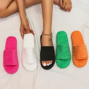 Detail of colorful fuzzy platform slide slippers with embossed patterns on white bed.