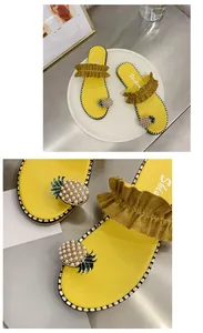 Close-up detail of yellow flat sandals with pearl pineapple decor and ruffled strap.
