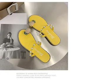 Flat yellow sandals featuring pearl straps and a decorative pineapple ornament