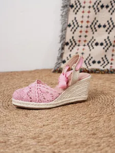 Vista lateral de sandalias con cuña de encaje rosa y detalle de suela de yute tejido.