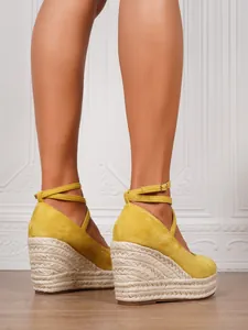 Primer plano de sandalias de cuña de ante amarillo con suela de cuerda trenzada y hebilla