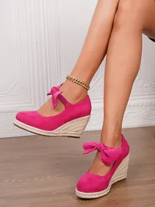 Primer plano de sandalias de cuña en ante rosa con lazo y plataforma de esparto