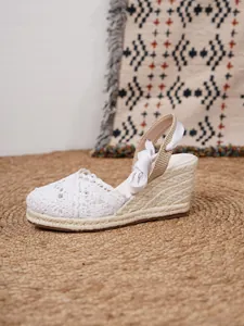 Elegantes sandalias de cuña de ganchillo blanco con suela de esparto y cintas.