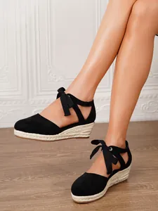 Primer plano de alpargatas de cuña negras con elegantes tiras de lazo al tobillo.