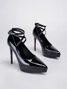 Detalle de zapatos de tacón en charol negro con plataforma y correas cruzadas al tobillo.