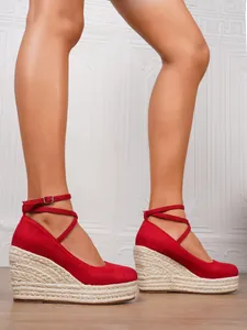 Detalle de sandalias de cuña de gamuza roja con elegante cierre de hebilla al tobillo