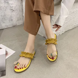 Close-up of yellow flat sandals featuring ruffle straps and pearl pineapple decor.
