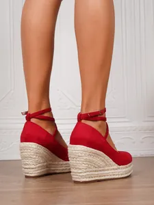 Detalle de sandalias de cuña rojas con plataforma de paja tejida y tira al tobillo