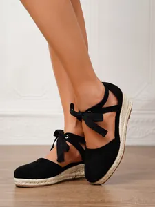 Detalle de alpargatas negras con cuña y lazo al tobillo en una modelo