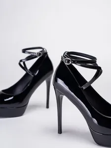 Detalle de tacones altos de charol negro con correas al tobillo y tacón de aguja