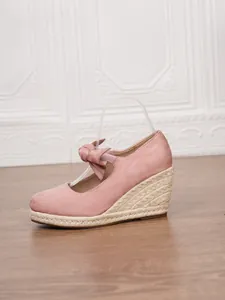 Sandalias de cuña de alpargata en ante rosa con lazo elegante y tacón de paja trenzada.