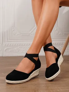 Vista detallada de sandalias de cuña negras con elegantes correas cruzadas en una modelo
