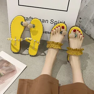 Detailed shot of trendy yellow flat sandals featuring pearl pineapple motifs and ruffles