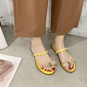 Close-up of yellow flat sandals featuring elegant pearl straps and a pineapple toe ornament
